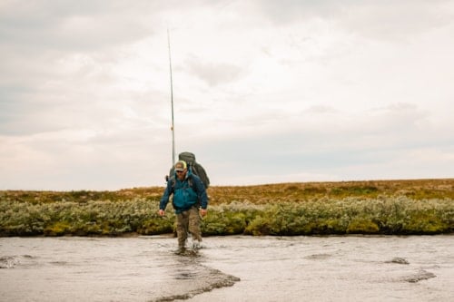 Mann med fiskeutstyr går over vannet på vidda.