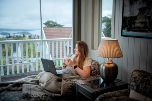 Dame sitter i sofaen og ser ut av vinduet med PC på fanget